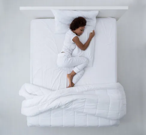 Hermosa mujer afroamericana tumbada en la cama durmiendo y abrazando una almohada, vista desde arriba.