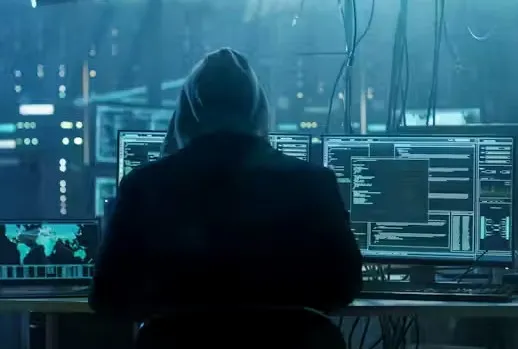 Hacker con capucha delante de varias pantallas con terminales de ejecución.